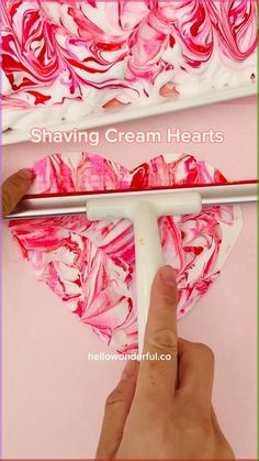 someone is painting pink and red swirled cream hearts on a white tray with the words shaving cream hearts above it