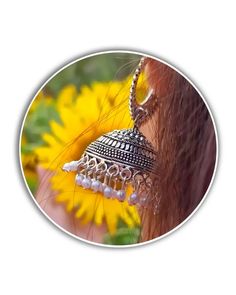 a close up of a person's ear with a bell on it and sunflowers in the background