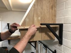 a man working on a piece of wood in a room with white brick walls and wooden shelves