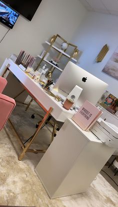 an apple computer sitting on top of a desk next to a pink chair and television