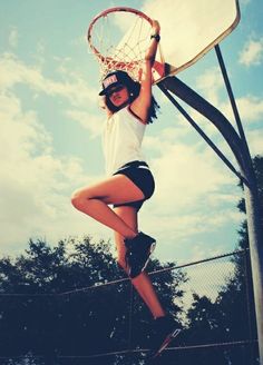 a woman is playing with a basketball hoop in the air while wearing shorts and a t - shirt