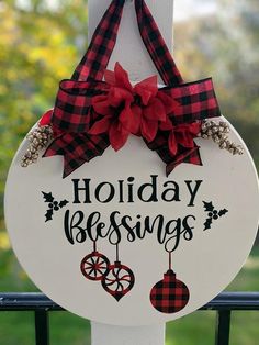 a holiday sign hanging on the side of a fence with red and black plaid bow