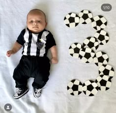 a baby is laying next to soccer balls on a sheet that has the number 3 in it