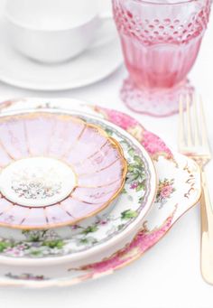 a table set with plates, silverware and pink glasses