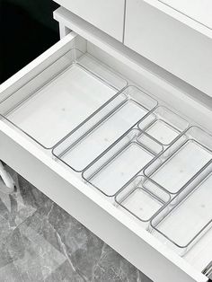 an open drawer with several trays in it on a marble countertop next to a white cabinet