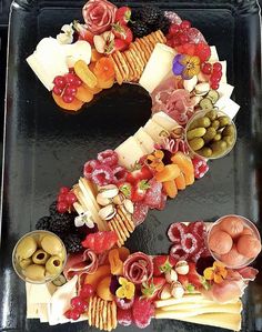 a letter made out of fruits and vegetables on a black tray with the number seven