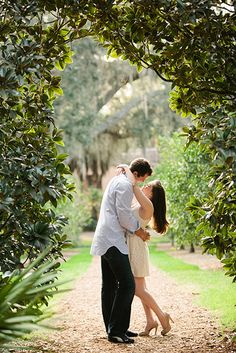 a man and woman are kissing in the middle of an apple tree lined path, surrounded by greenery