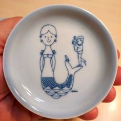 a hand holding a blue and white plate with a drawing on it