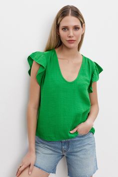 A woman with long blonde hair stands against a white wall Textured Top For Spring Layering, Spring Green Tops With Crinkle Texture, Green Crinkle Texture Top For Spring, Green Crinkle Texture Tops For Spring, Chic Cotton Tops With Crinkle Texture, Casual Textured Summer Blouse, Spring Cotton Top With Crinkle Texture, Spring Cotton Crinkle Texture Top, Casual Tops With Crinkle Texture For Layering