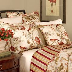 a bed with red and white flowers on it next to a framed painting in a bedroom