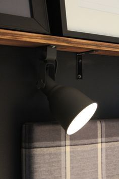 a black lamp is on the wall next to a gray couch with a checkered pillow