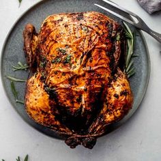 a roasted turkey on a plate with rosemary garnish and a knife next to it