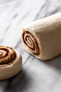 two cinnamon rolls sitting on top of a marble counter next to each other, with one rolled up in the middle