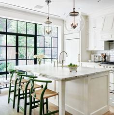 a white kitchen with an island in the middle and two stools at the end