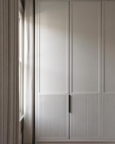 a white closet with two doors and some curtains on the window sill in front of it