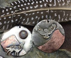 two metal discs with different designs on them next to a feathers feather and some beads