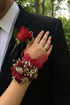 a close up of a person wearing a suit and holding a red rose wrist corsage