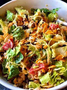 a salad with lettuce, tomatoes, cheese and other toppings in a white bowl