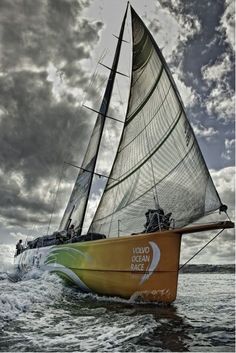 a yellow sailboat with white sails in the ocean on a cloudy day, under dark clouds