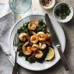 a white plate topped with shrimp, spinach and lemon wedges next to a glass of water