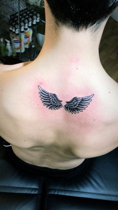 the back of a woman's neck with an angel wing tattoo on it