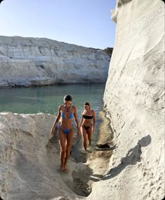 two women in bikinis are walking through the water near some cliffs and white cliffs