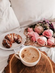 a cup of coffee and some doughnuts on a tray with pink roses in the background