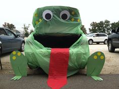 a large green frog sitting on top of a parking lot