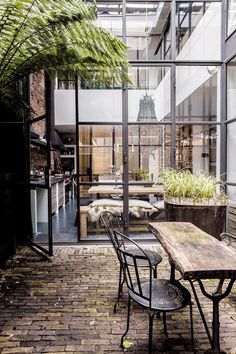 an outdoor dining area with wooden tables and chairs, surrounded by large glass windows that look out onto the courtyard