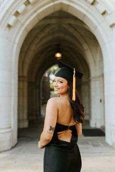 a woman wearing a graduation cap and gown standing in front of an arched archway with her hand on her hip