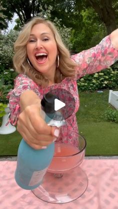 a woman holding a blender and pointing at the camera with her right hand, on a pink table cloth