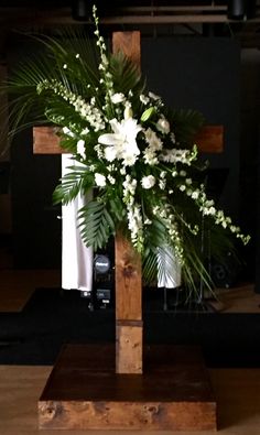 a wooden cross with white flowers and greenery