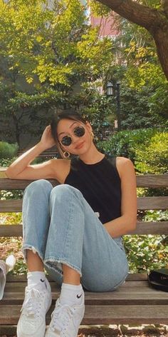 a woman sitting on top of a wooden bench next to a park filled with trees