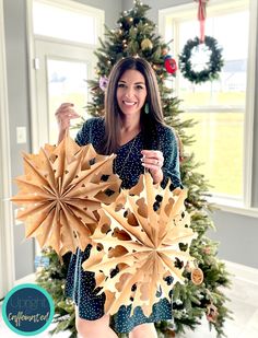 a woman holding up two paper flowers in front of a christmas tree with other decorations