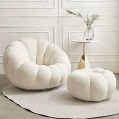 two white chairs and a table with a plant on it in front of a wall