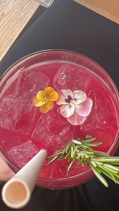 a person is holding a drink with flowers on the rim and garnished with rosemary