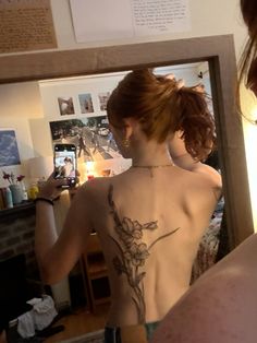 a woman with a tattoo on her back taking a selfie in front of a mirror