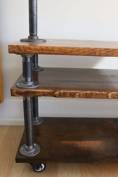 three wooden shelves with metal pipes on each shelf and wood flooring in the background