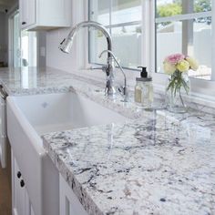 a kitchen with marble counter tops and white cabinets, flowers in the window sill