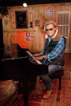 an older woman sitting at a piano in a room with wood paneling on the walls