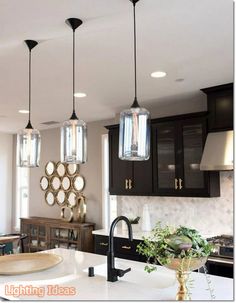 a kitchen with black cabinets and lights hanging from it's ceiling above the island