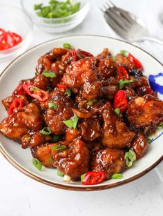 a white plate topped with chicken covered in sauce and green onions next to silverware