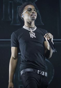 a man in black shirt holding a microphone and wearing headphones on his ears while standing next to a stage