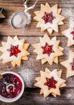 some cookies with jam on them are sitting next to a bowl and cookie cutters