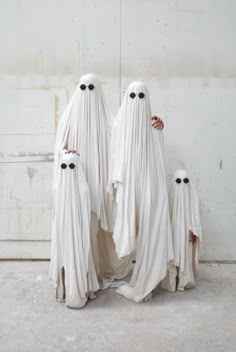 three white ghost statues standing next to each other with black eyes on their faces and arms