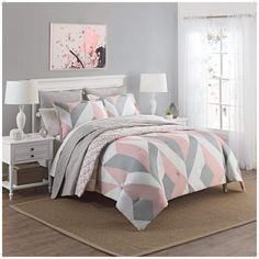 a bed with pink and grey comforter in a bedroom next to a white dresser