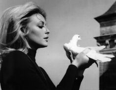 a woman holding a white bird in her right hand and looking at it's side