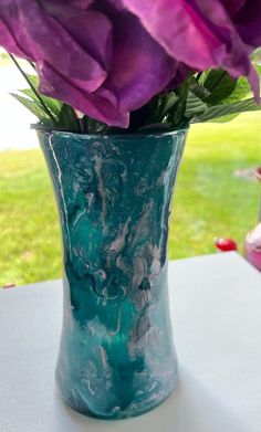 purple flowers are in a blue vase on a table outside with green grass behind it