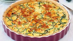 a quiche with zucchini and cheese in a red dish on a white tablecloth