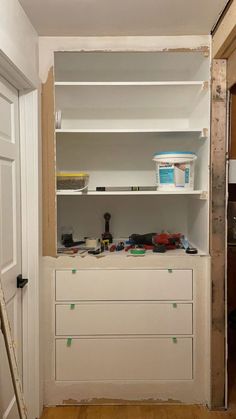 an unfinished room with shelves and tools on the floor, next to a door that has been painted white